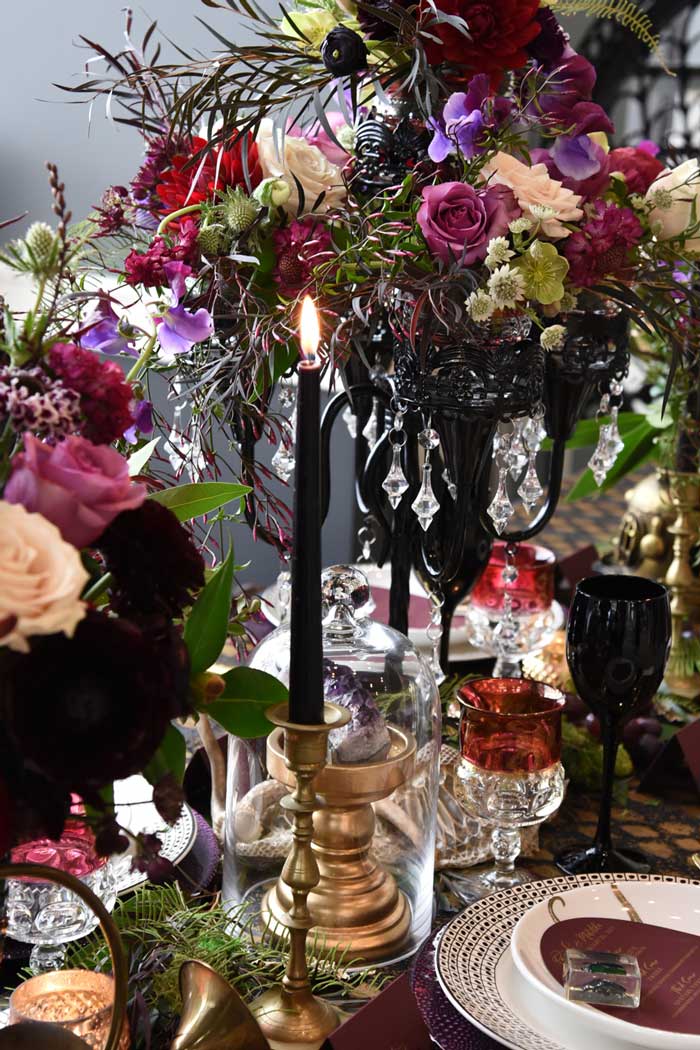 Halloween tablescape featuring dark and textural flowers, black tapers, and red and black goblets.