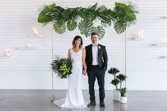 Cute wedding couple in front of modern tropical wedding arch with acrylic accents