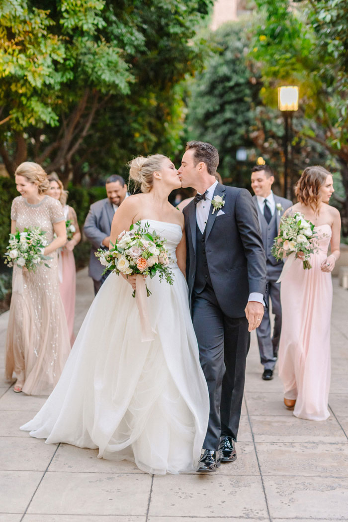 Cute wedding couple kissing, while walking with bridal party in DTLA.