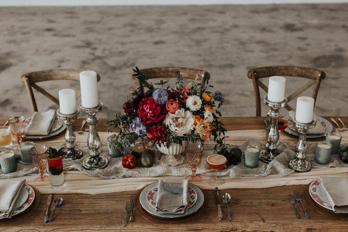 Romantic and Moody tablescape featuring a lush centerpiece of peonies, dahlias, and ranunculus, lots of candles, and beautiful cocktails.