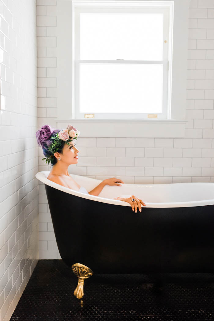 Unicorn mama-to-be in a black clawfoot bath tub surrounded by white subway tile.