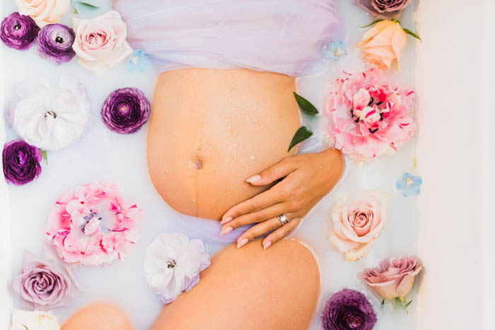 Preggo belly in a milky bath surrounded by blush and lavender flowers.