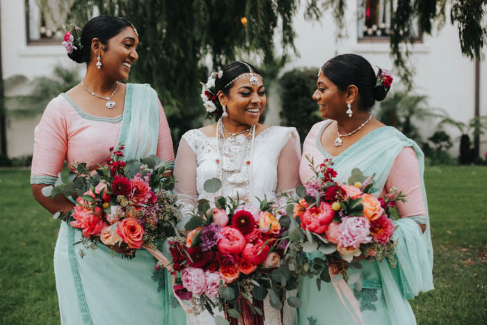 Beautiful bride and bridesmaids in white, peach, and mint saris carrying bold, colorful, and luxurious blooms.