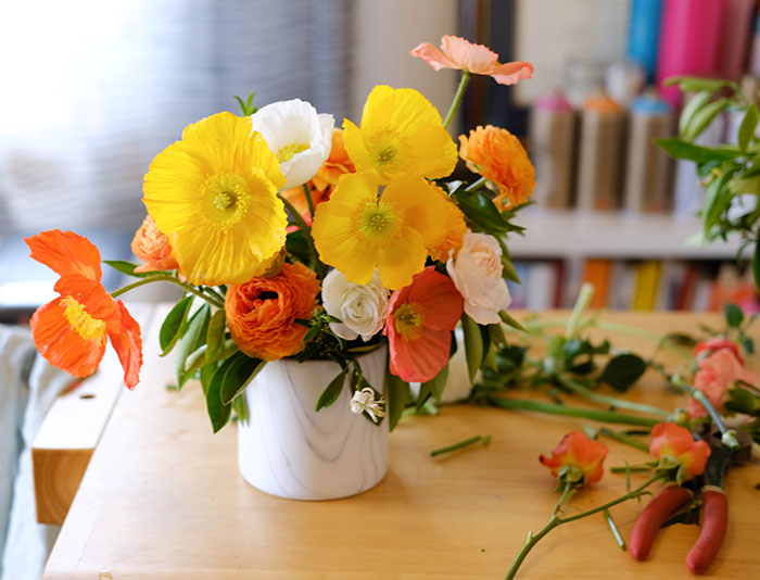 Beautiful arrangement by Winston & Main of yellow, orange, and white icelandic poppies and ranunculus in white marble vessel