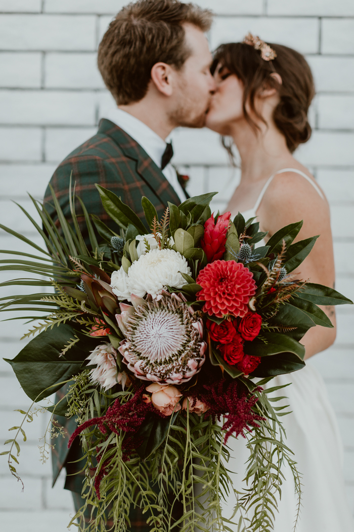 A sweet Los Angeles couple celebrate at their romantic wedding holding a tropical cascade bouquet full of dahlias, garden roses, protea, and blushing bride protea.