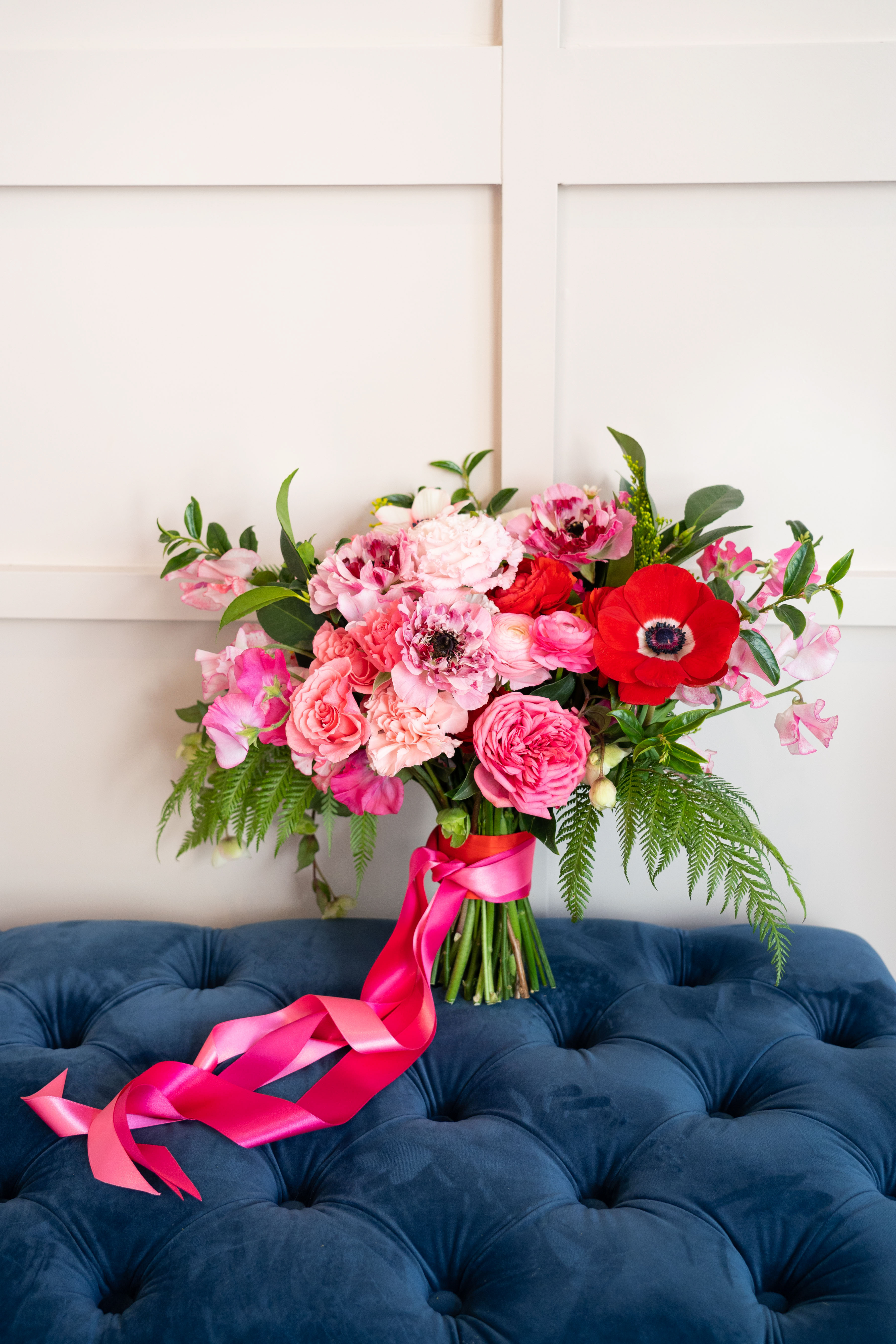 The lush bridal bouquet featuring vibrant red and pink ranunculus, anemones, and peonies.