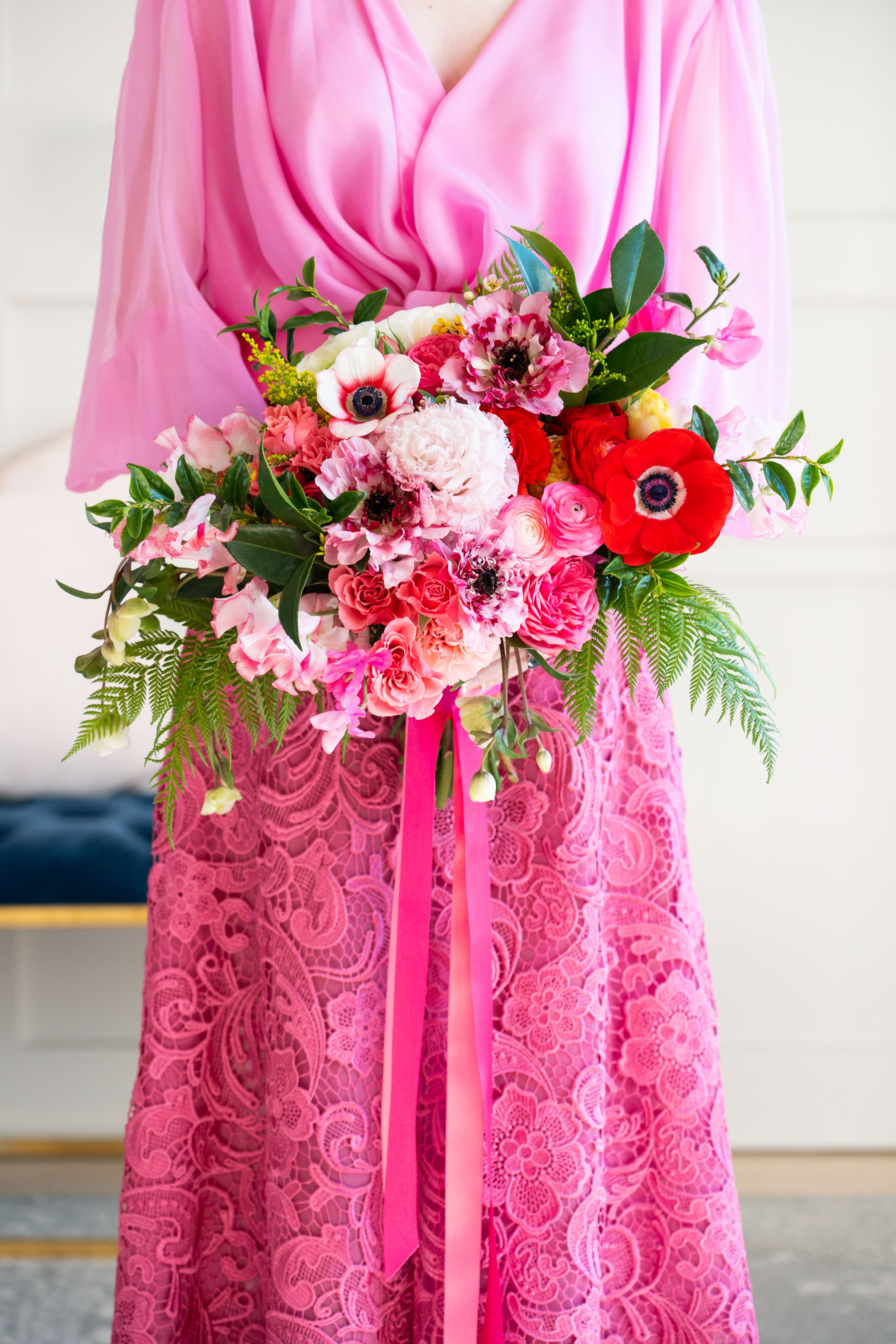 Our bride in a vibrant pink lace wedding dress, holding her lush bridal bouquet full of bright ranunculus and anemones.