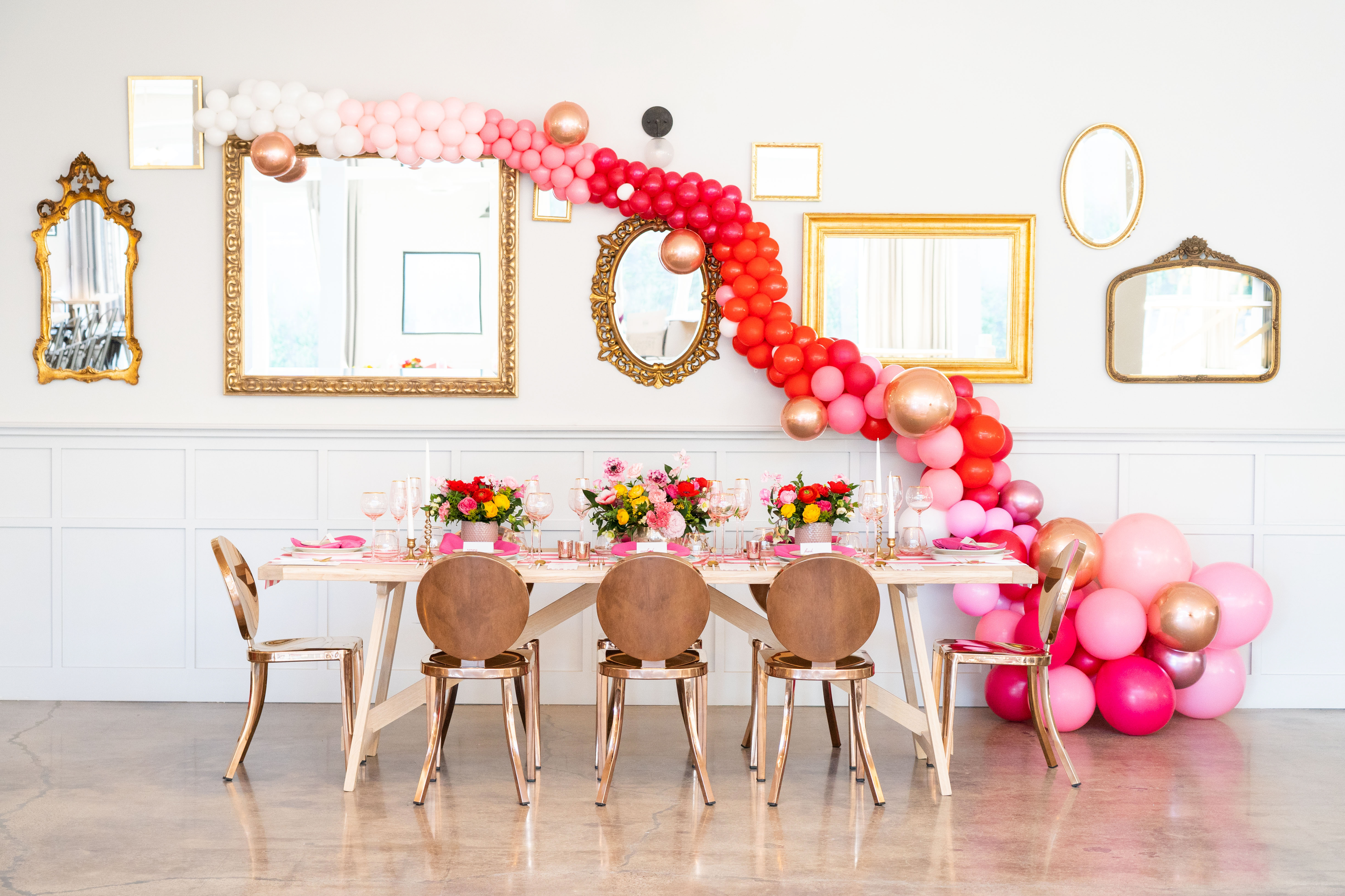 The quirky Valentine's Day-themed reception space featuring a vibrant balloon installation, vintage gold hanging mirrors, and lush yellow and red flower table arrangements by Winston and Main. 