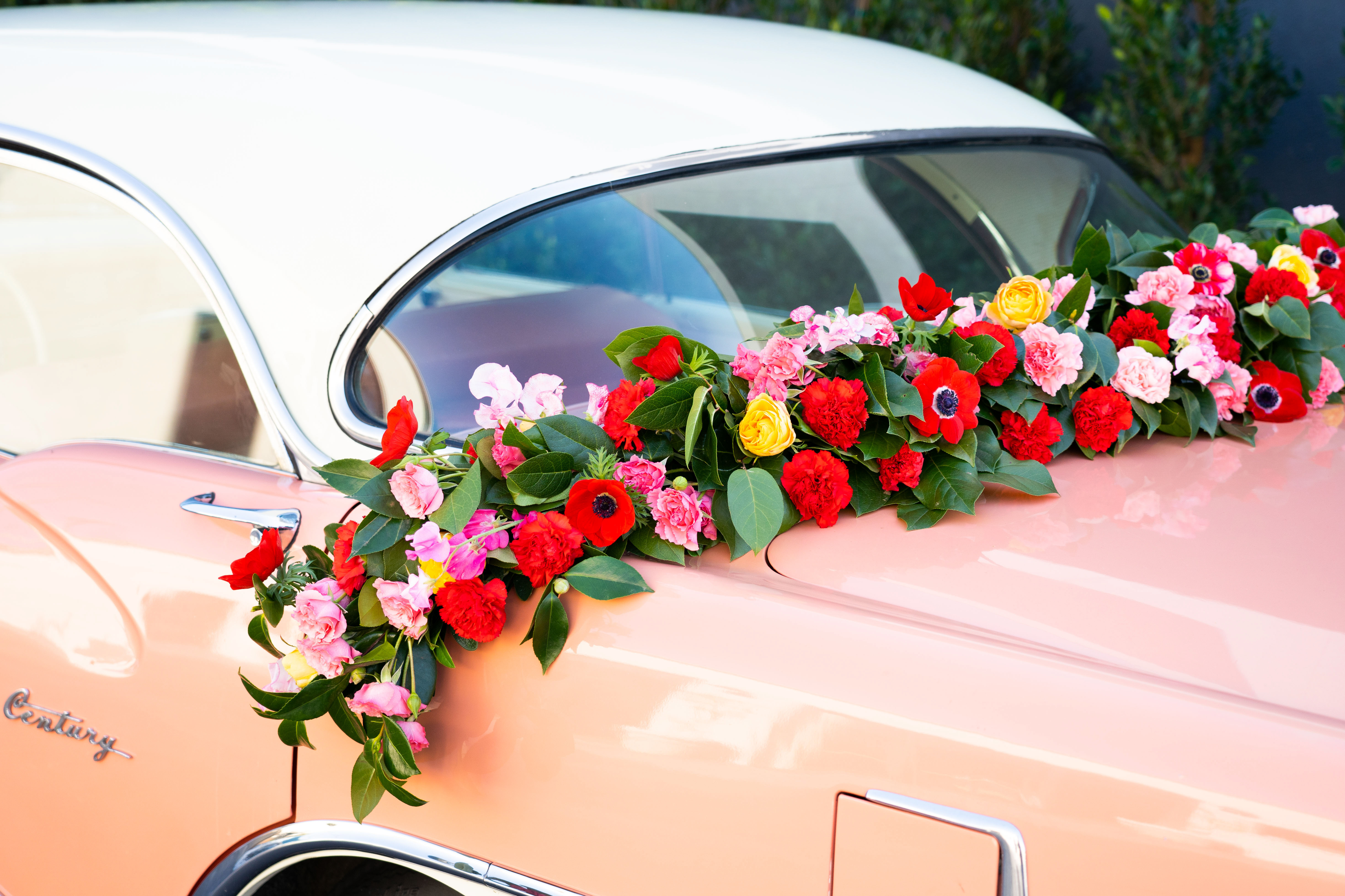 Our vibrant red, yellow, and pink garland adorning the couple's peach vintage getaway car.