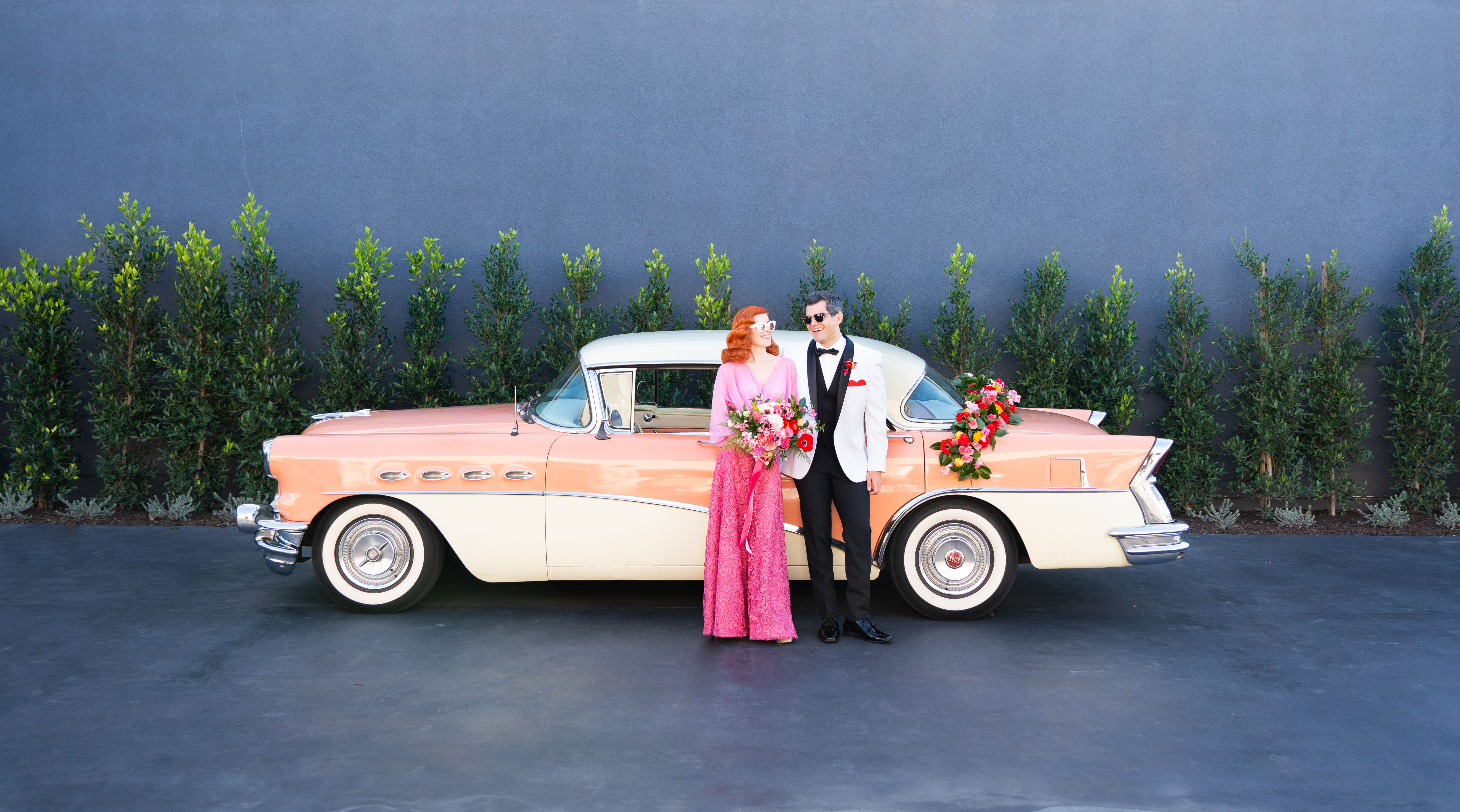 Our quirky sweet couple styled in retro wedding attire to compliment their vintage getaway car a lush red and pink garland to match the vibrant bridal bouquet.