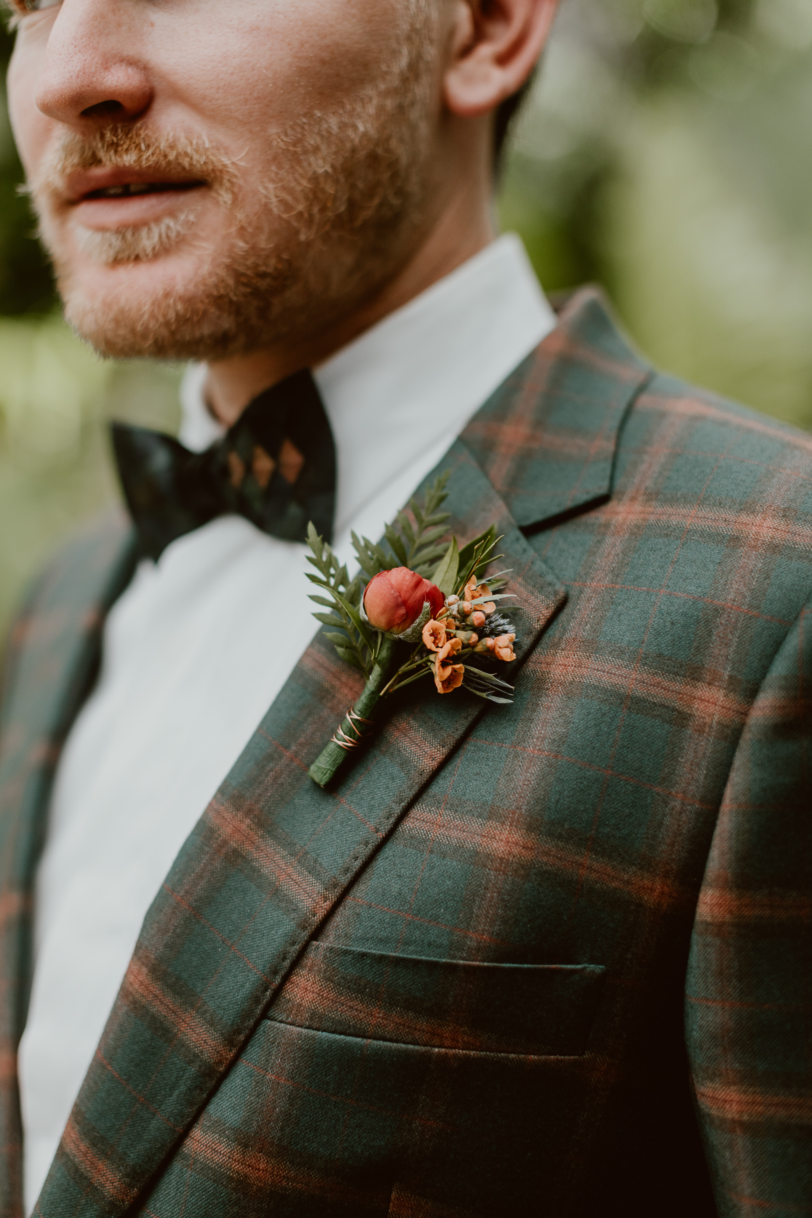 Our groom's boutonniere features a red ranunculus, thistle, and orange wax to match his tartan suit.
