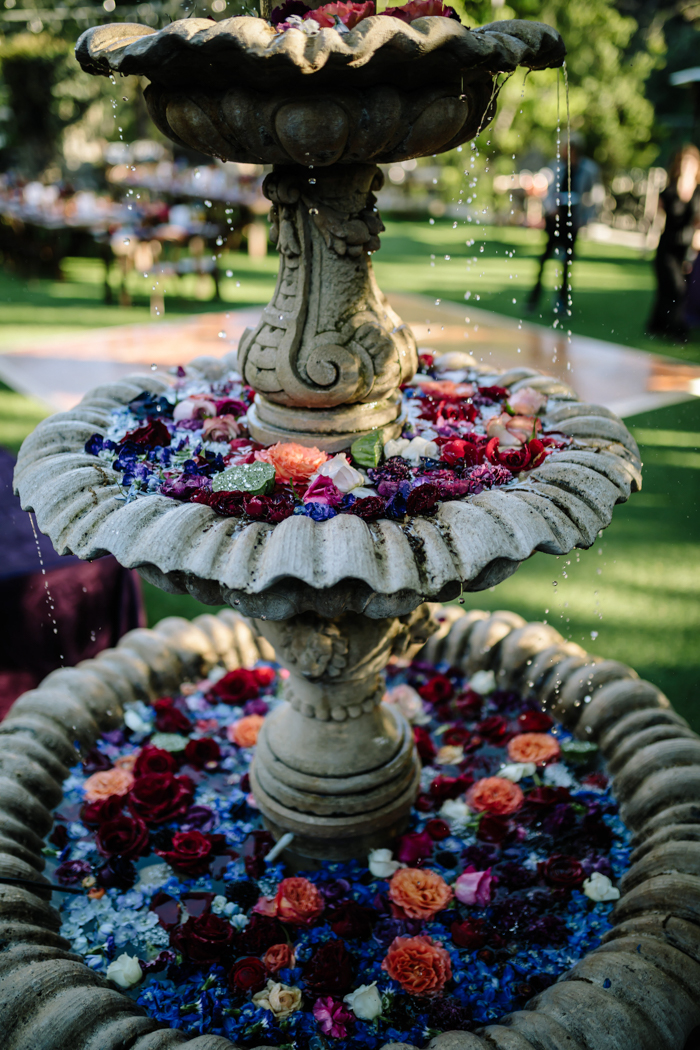 Houdini Estate's water fountain decorated with moody jewel toned petals and buds by Winston and Main.