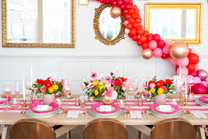 A brilliant Valentine's Day tablescape featuring pink Japanese ranunculus and red anemones with a balloon garland backdrop.