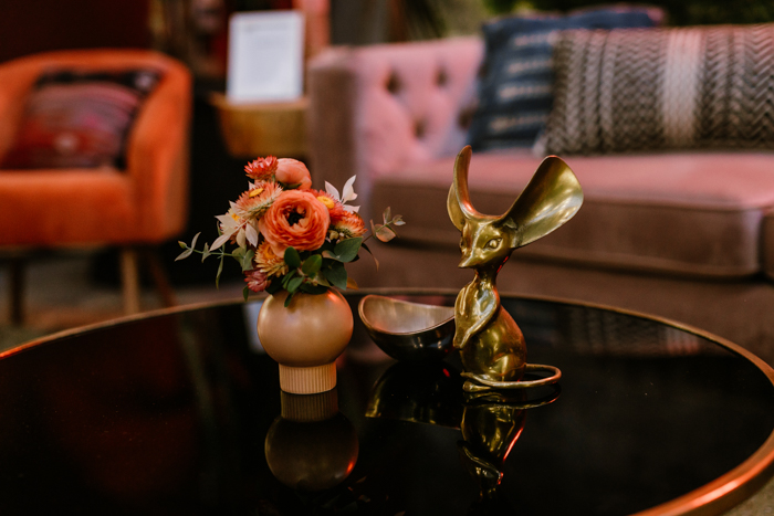 A petite red floral arrangement, perfect for a cocktail hour, sits on a coffee table with a brass mouse statue.