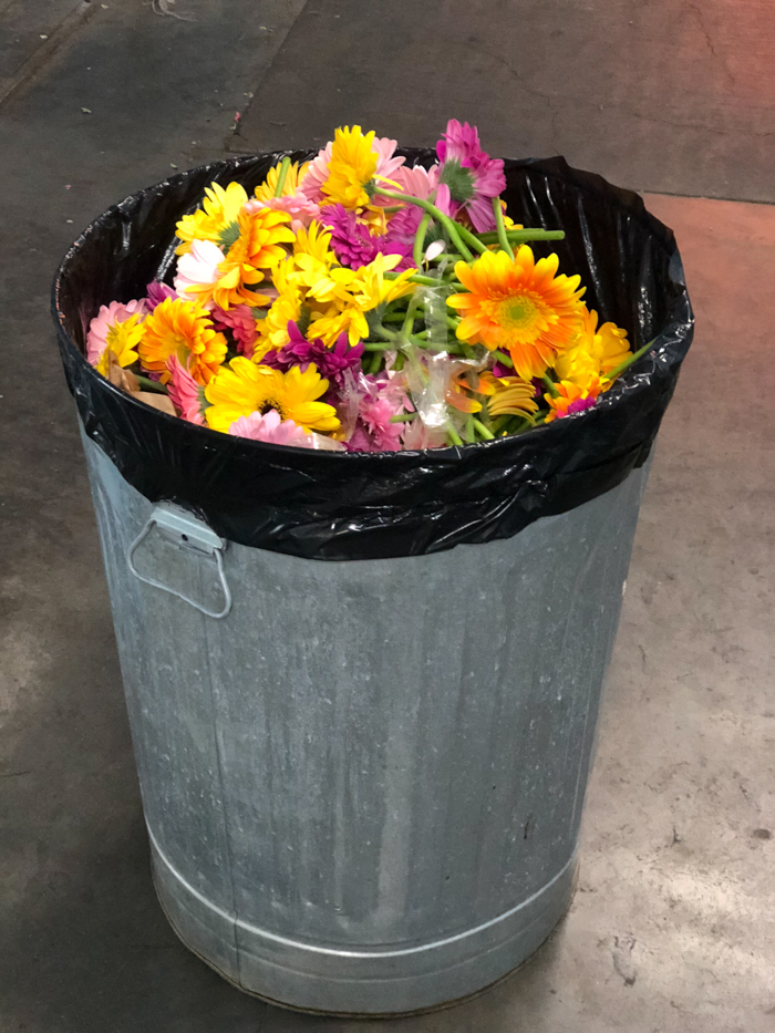 A trash can full of brightly colored flowers, following an event. 