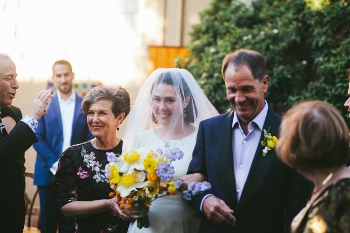 In Jewish wedding tradition, both the bride’s parents walk her down the aisle, as she holds her airy, organic, and whimsical bouquet which features Claire de Lune Peonies. 