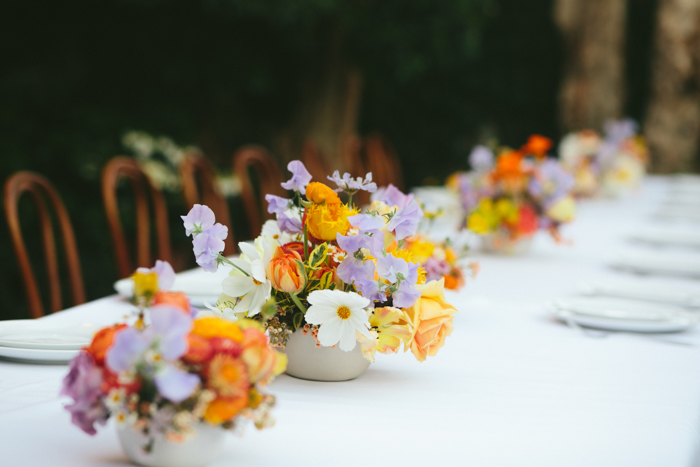 A lush wedding tablescape designed by Winston & Main features multiple arrangements full of local flowers like peonies, garden roses, cosmos, sweet pea and ranunculus, mixed with beautiful pillar candles down the length of the tables.