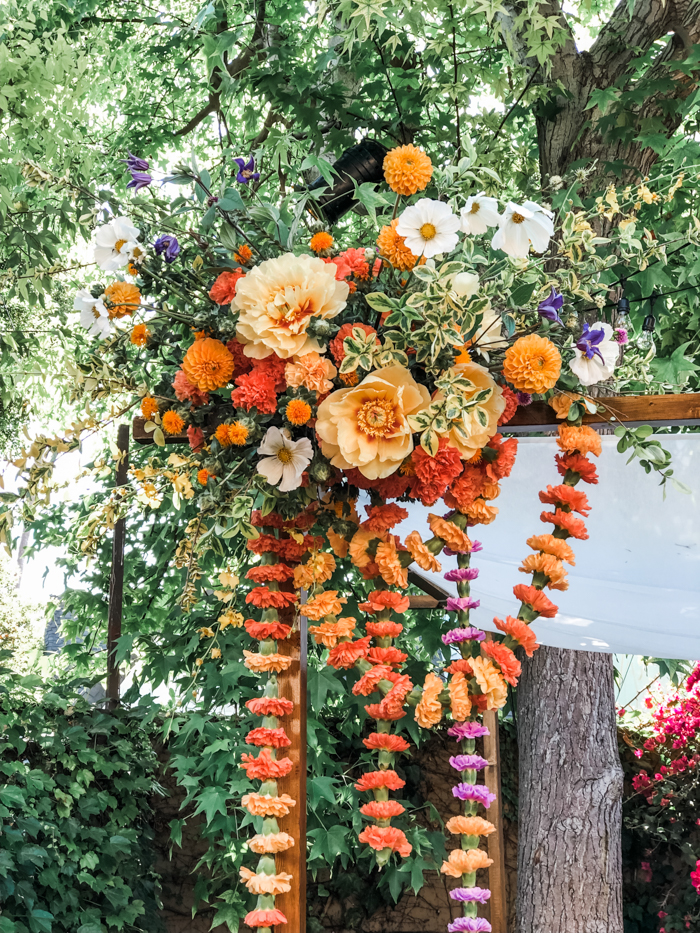 A detail shot of Winston & Main’s Chuppah floral installation in monochromatic shades of orange/peach that features peonies, poppies, marigold, cosmos and whimsical carnation garlands.