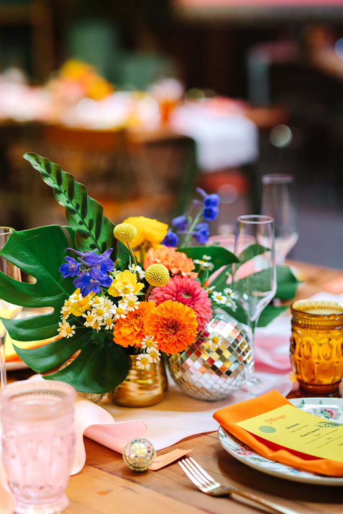 Bold, colorful, & tropical centerpieces featured pink and orange dahlias, a touch of cobalt, and mixed tropical greenery.