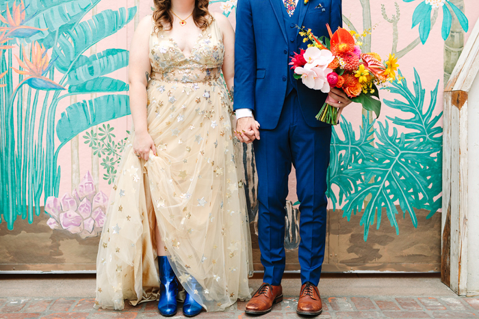 A portrait of the stylish couple: The bride wore cobalt blue boots and the groom holds her colorful tropical bouquet. 