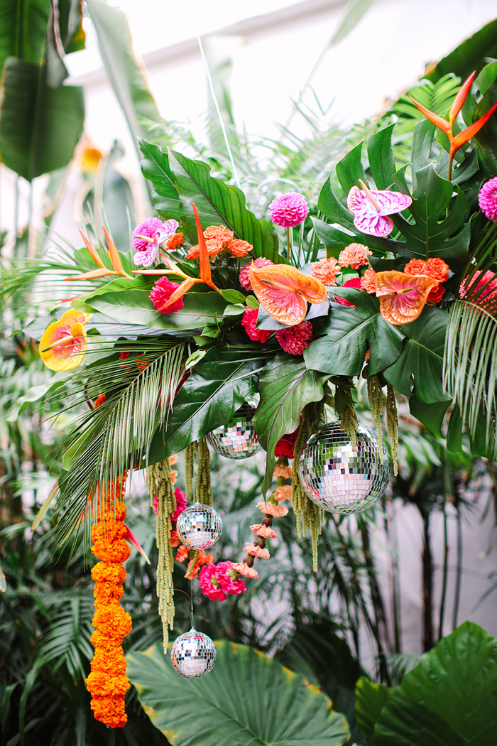 This hanging tropical floral installation served as the wedding arch and was created without floral foam. It features anthuriums from Haus of Stems, alongside bold blooms, disco balls, and festive carnation and marigold garlands.