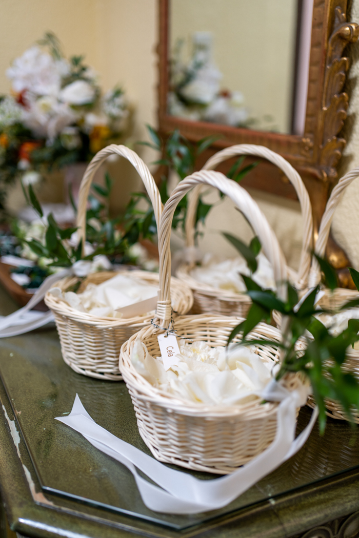 Adorable flower child baskets, accented with greenery and filled with fresh white rose petals for tossing.