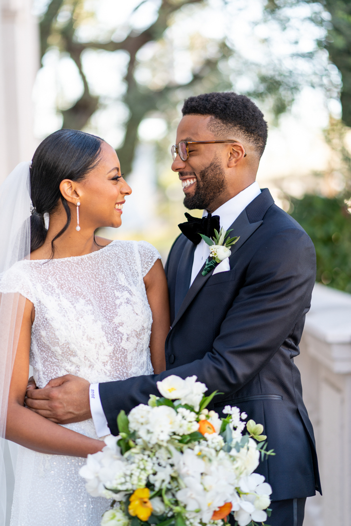 The couple smiling at each other with groom gently holding her waist, and bride holding a lush white and citrus accented bouquet designed by Tabitha Abercrombie of Winston & Main.