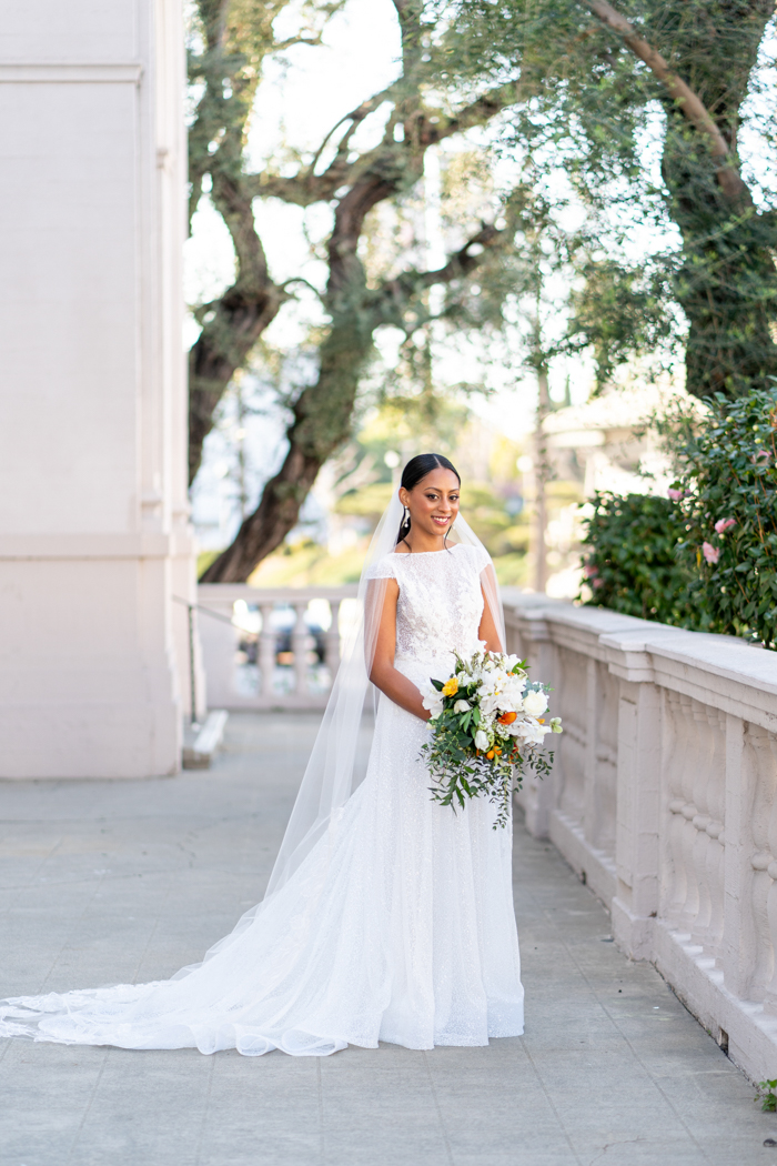 An outdoor portrait of our bride holding a luxury bouquet with white flowers, accented by fresh citrus, and yellow and orange blooms.