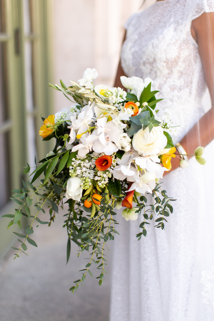 A lush and organic white cascade with pops of orange and yellow accents, featuring garden roses, peonies, ranunculus blooms, designed by Winston & Main.