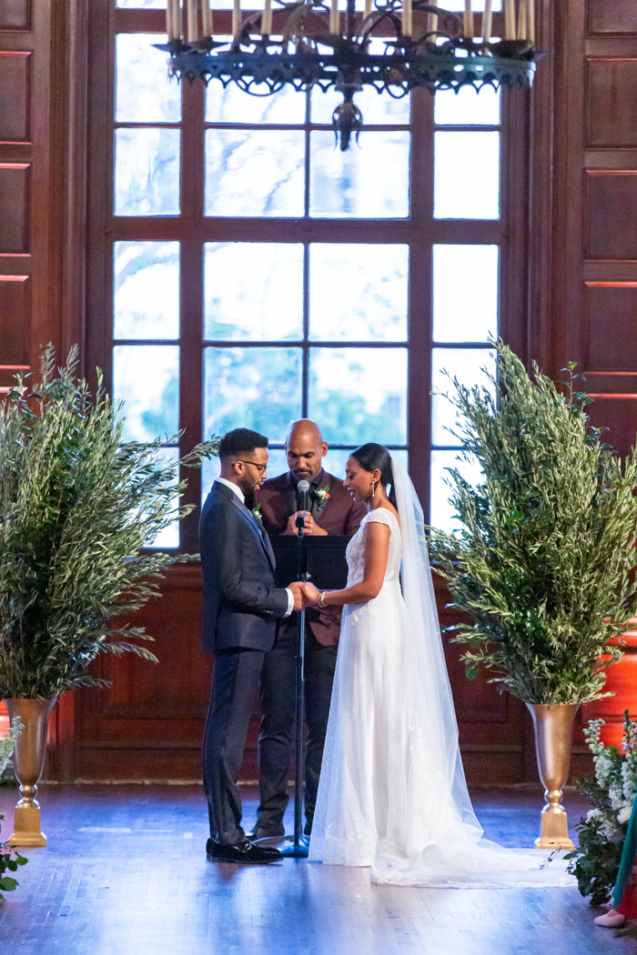 The couple and their officiant stand in between two large, foam-free installations featuring olive and eucalyptus branches in gold urns.