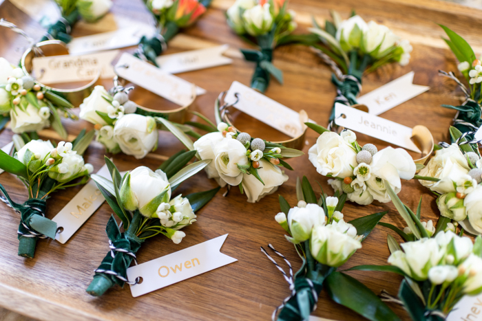 A close up of boutonnières and brass cuff corsages made of white flowers on a tray, custom designed by Winston & Main.