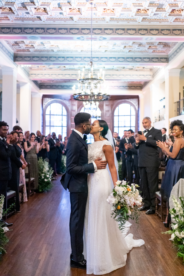 The couple's first kiss with guests cheering on while our bride holds on to the luxury bouquet, designed by Winson & Main, at her side.