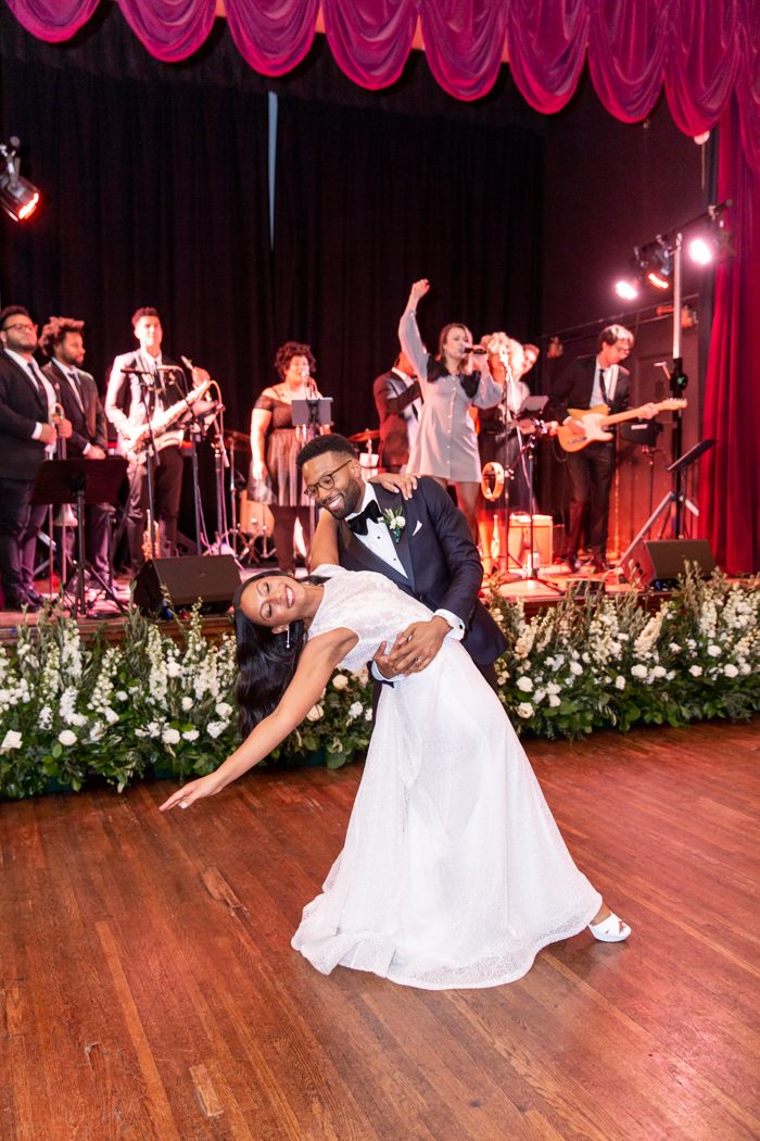 A dramatic first dance is set against a lush green and white floral installation at the base of the stage. 
