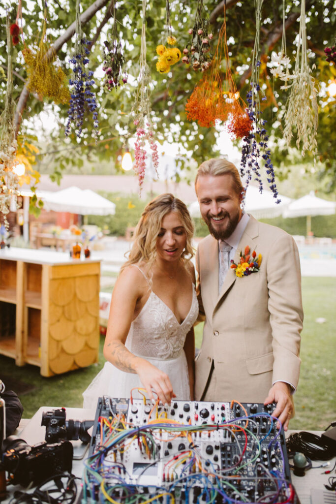 Our music-loving couple having a playful moment with DJ's equipment under an eco-friendly installation of hanging bouquets of dried flowers!