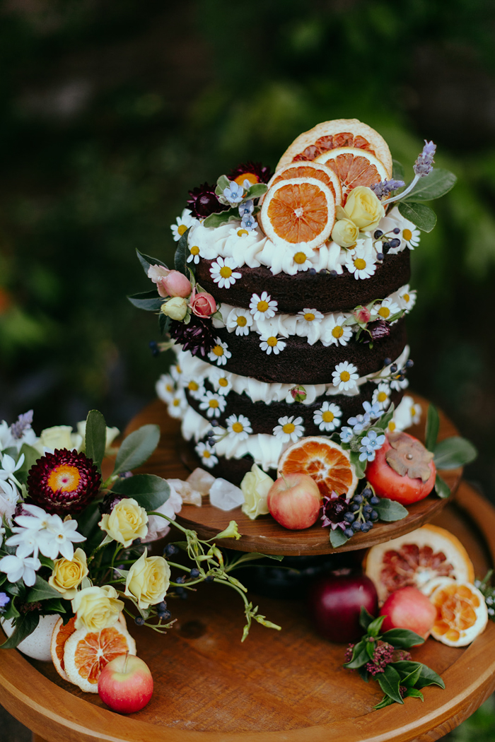 A chocolate naked cake by Nicole Bakes Cakes is adorned with fresh florals, chamomile blooms, and citrus accents.