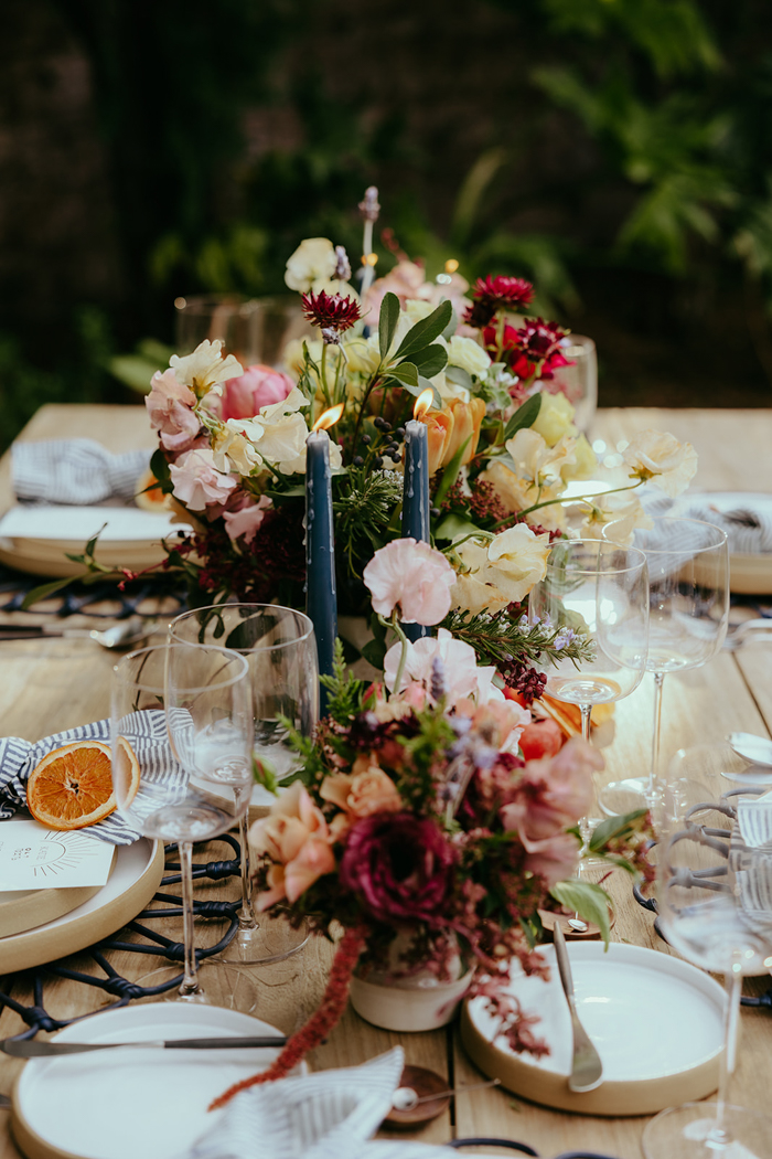 A moody, lush, and abundant table scape featuring local blooms in shades of lemon yellow, blush and burgundy with blue accents and taper candles.