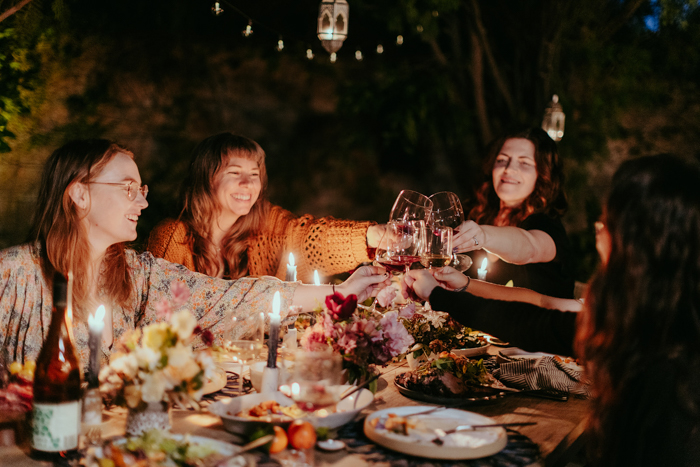 Event pros enjoy a candlelit dinner party, toasting with wine over a table full of family style dinner.