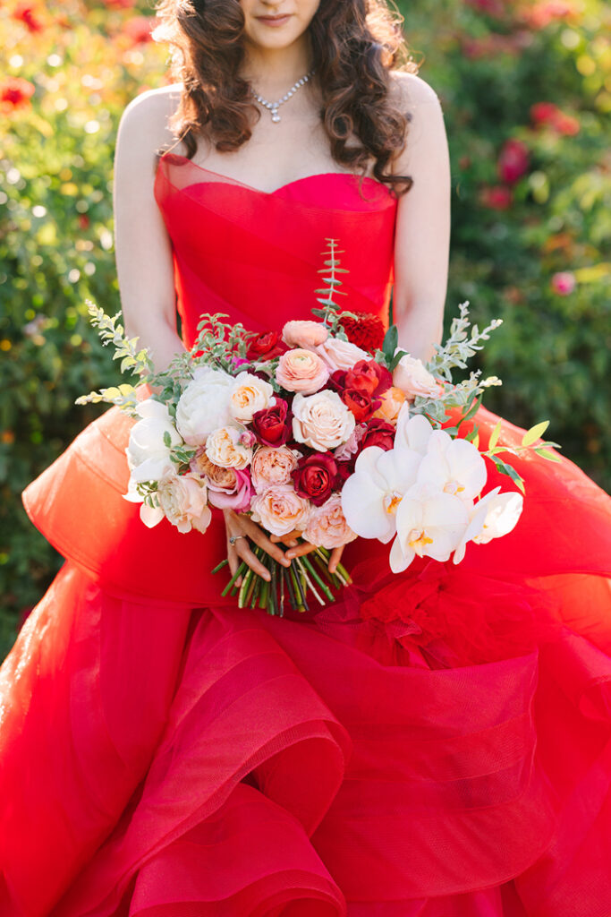 A portrait of a bride wearing a red wedding dress holding an elegant bouquet of red garden roses and cream flowers.