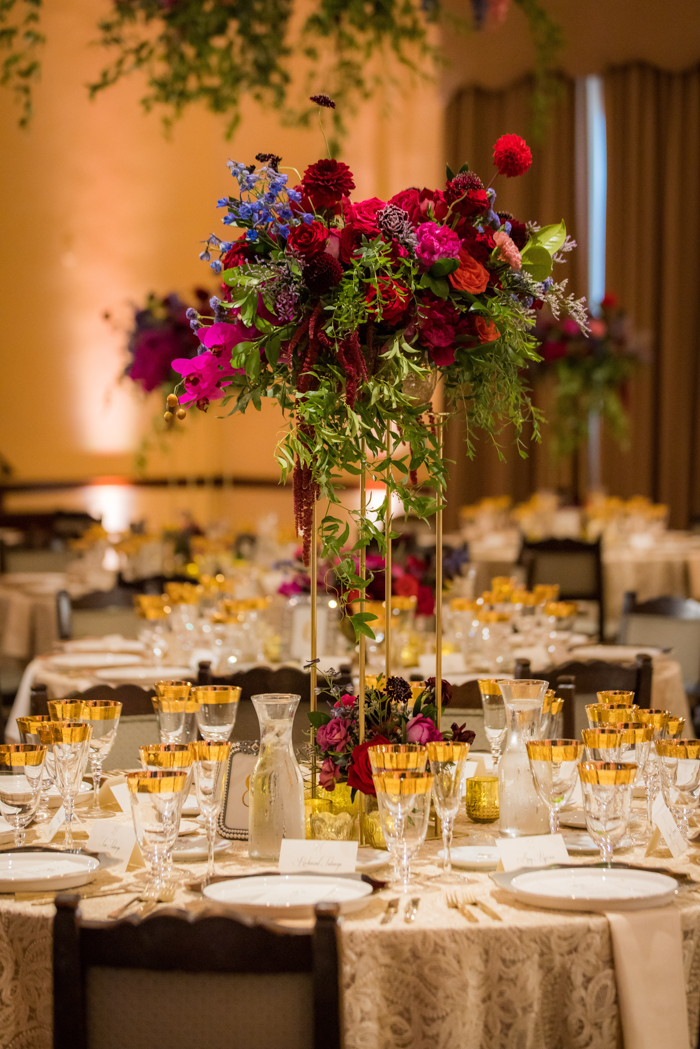 A lush jewel-toned elevated wedding centerpiece full of peonies, orchids, dahlias, and delphinium.