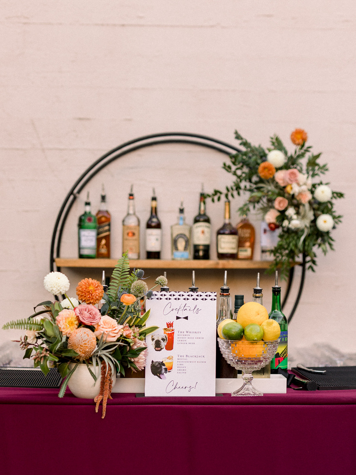 A custom cocktail menu featuring the couples dogs is displayed beside an organic arrangement on the bar and features a custom site specific floral installation on the back bar in shades of blush, peach, coral and orange. 