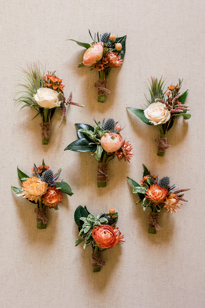 Textural boutonnieres by Los Angeles event florist, Winston & Main composed of ranunculus, spray roses, airplants, strawflower and thistle in shades of peach, corals, and orange.