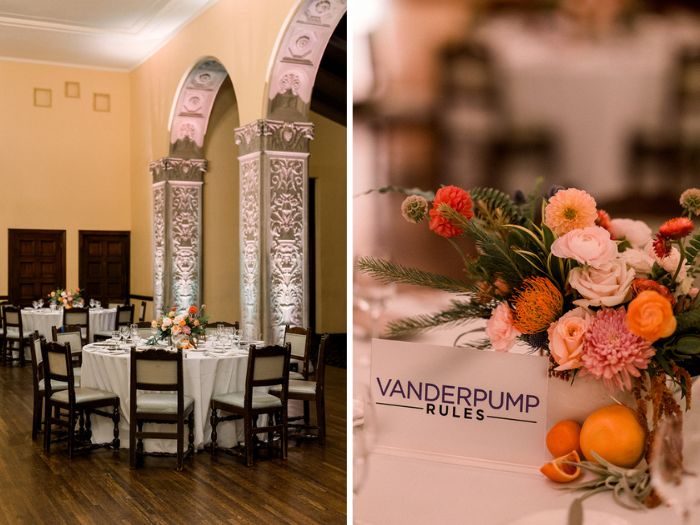 The wedding reception details include large citrus-hued centerpieces full of dahlias and garden roses and acrylic table numbers showing the couples favorite TV shows are set against the dramatic arches in the dining room at historic California wedding venue, The Ebell of Los Angeles.
